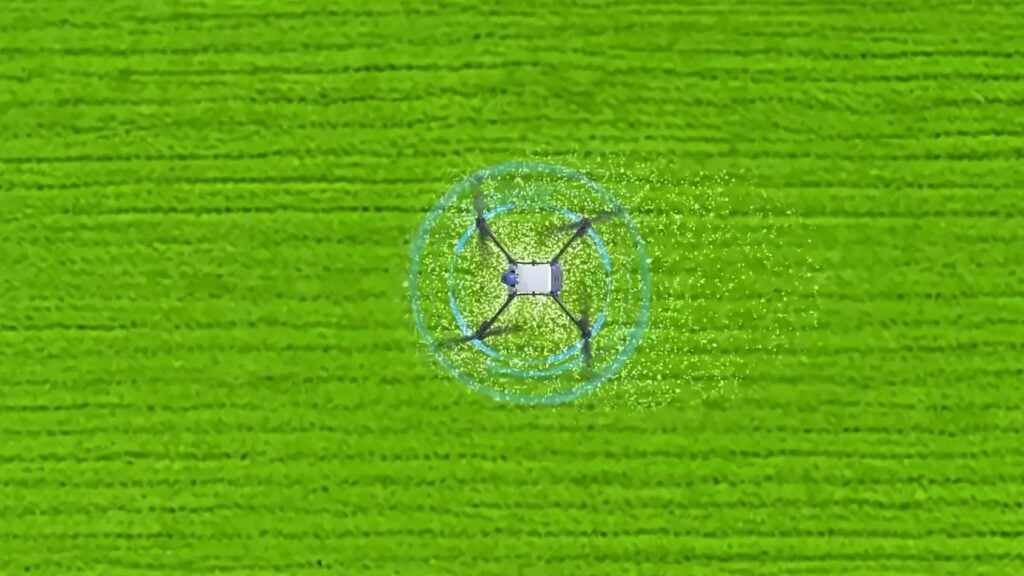Aerial view of a drone spraying a green agricultural field.