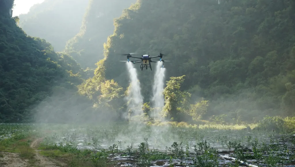 Agricultural J100 spraying drone flying over a field in a lush green valley.